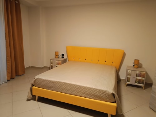 Camera moderna a Domus Smartrooms a Sellia, Italia con letto imbottito giallo, biancheria beige, comodini e atmosfera calda