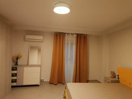 Camera moderna presso Domus Smartrooms Sellia con letto matrimoniale, tende arancioni e illuminazione ambientale al soffitto