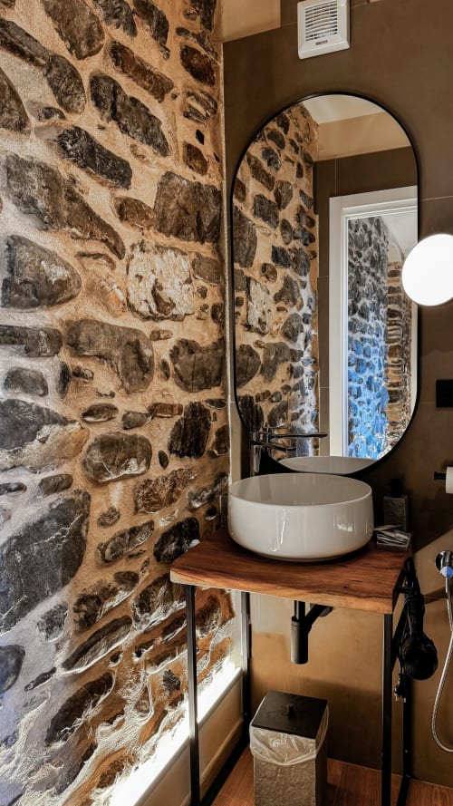 Moderno bagno della Talking Stones B&B a Dolceacqua con muro in pietra, lavabo bianco e specchio rotondo