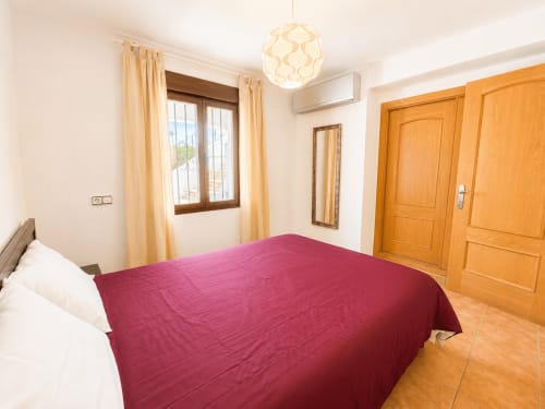 Dormitorio espacioso con ropa de cama burdeos, armario de madera y vistas a la terraza en la villa Casa Jonur, Moraira