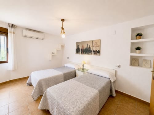 Luminoso dormitorio doble en villa Casa Jonur, Moraira: dos camas, paredes blancas, estanterías empotradas y cuadros de la ciudad