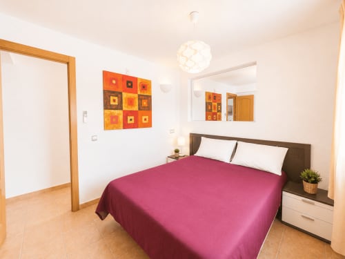 Dormitorio moderno y luminoso en la villa Casa Jonur de Moraira con ropa de cama rosa, cabecero marrón y vibrante arte naranja
