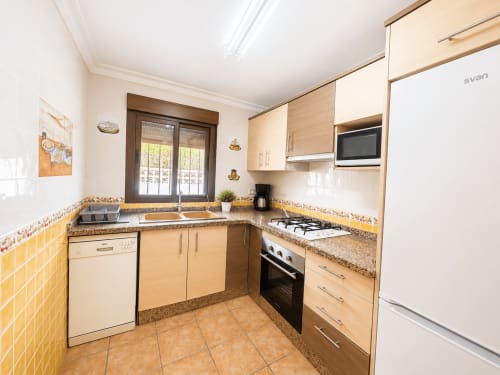 Cocina moderna con azulejos amarillos, encimeras de granito, estufa a gas y puertas de madera oscura hacia patio en Casa Jonur