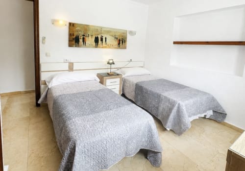Dos camas individuales con colchas grises en una habitación luminosa de la villa Casa Jonur en Moraira, con cabecero blanco y detalles de madera