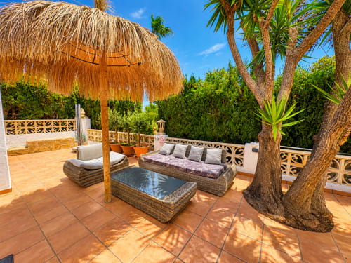 Terraza de villa en Moraira con asientos de mimbre, sombrilla de paja, árboles maduros y vistas al mar en Moraira, España