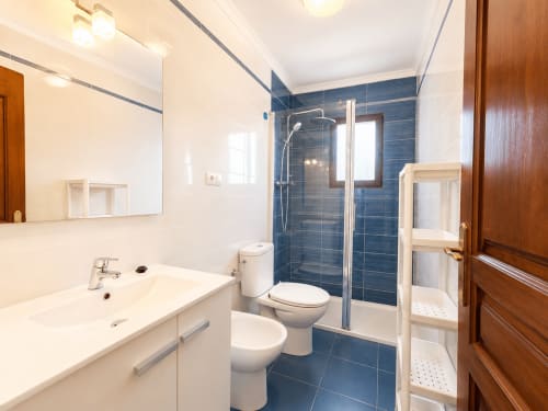Moderno baño en villa Casa Jonur con lavabo blanco, ducha con azulejos azules, inodoro y puerta de madera en Moraira Rental Villas