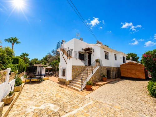 Villa Casa Jonur en Moraira con fachada blanca, escaleras de piedra, terraza y exuberantes jardines mediterráneos bajo cielo azul