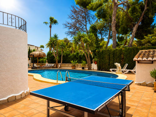 Mesa de ping pong azul junto a la piscina de la villa Casa Jonur en Moraira, con tumbonas y palmeras