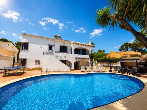 Casa Jonur villa in Moraira with oval pool, white Mediterranean-style building, palm trees, and sunny terrace with loungers