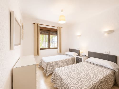 Luminoso dormitorio doble con ropa de cama beige en villa Casa Jonur de Moraira, con vistas al jardín y comodidades modernas