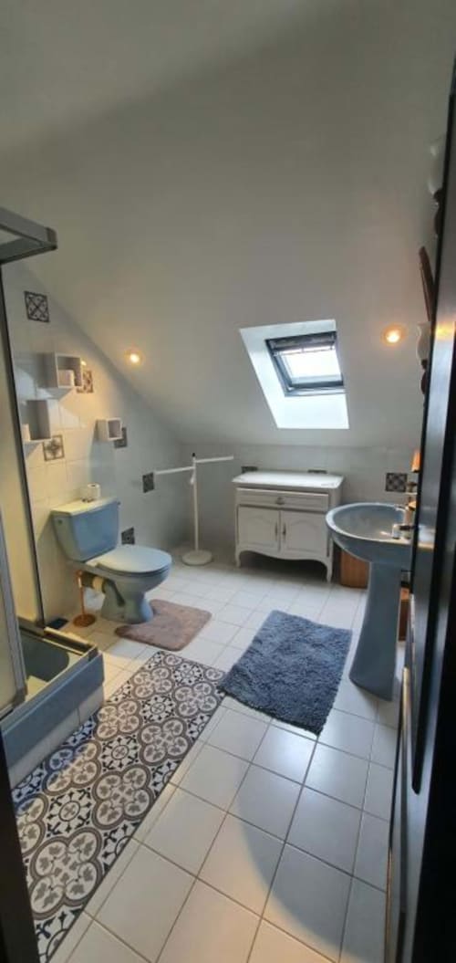 Salle de bain mansardée moderne au Manoir de Saint-Ouen avec lucarne, toilettes, lavabo sur pied, meuble blanc et tapis à motifs