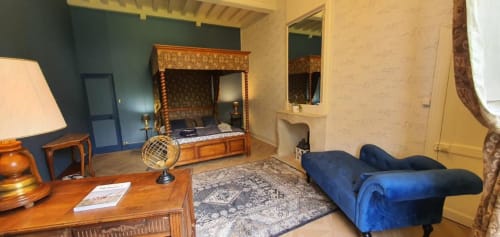 Élégante chambre du Manoir de Saint-Ouen avec lit à baldaquin, canapé en velours bleu et mobilier d'époque