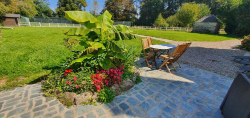 Terrasse en brique du Manoir de Saint-Ouen avec chaises en bois, fleurs rouges et jardins soignés à Sideville