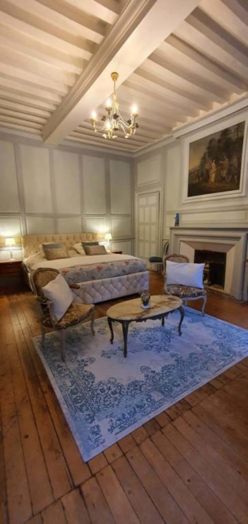Suite élégante du Manoir de Saint-Ouen avec plafond à caissons, cheminée et coin salon avec tapis bleu