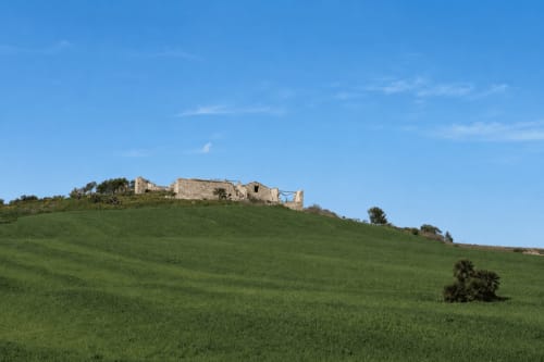 Rovine di un castello medievale sulla collina verde e ondulata vicino a Valderice, Sicilia, con cielo blu limpido