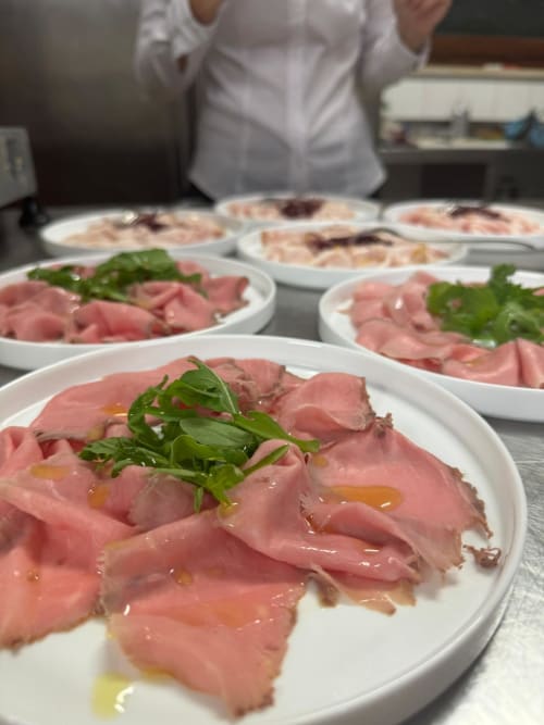 Sliced prosciutto with arugula and olive oil on white plates at Hotel Ristorante alle Querce in Castelbuono