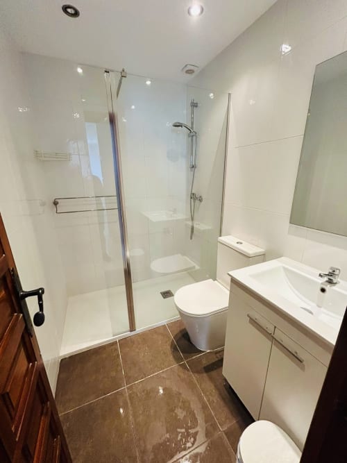 Baño moderno en Nerja Holiday Homes con mampara de ducha de cristal, vanidor blanco, inodoro y piso de azulejos marrones