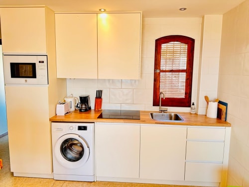 Cocina moderna en apartamento de Nerja Holiday Homes con muebles blancos, encimera de madera, lavadora, fregadero y placa de cocción