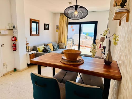 Comedor moderno en Nerja con vistas al mar, mesa de madera, sillas color turquesa y luminaria colgante negra contemporánea