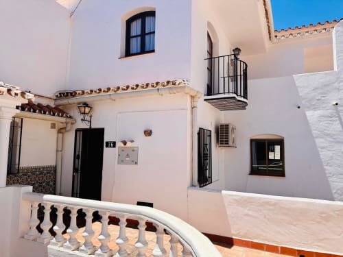Exterior de apartamento mediterráneo blanco en Nerja con terraza, ventanas arqueadas y persianas de madera oscura