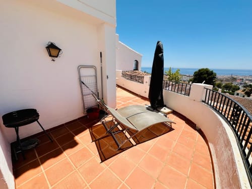 Soleada terraza de lujoso apartamento en Nerja con vistas al mar, tumbonas, sombrilla y paisaje costero