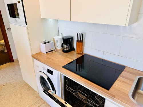 Cocina moderna con encimera de madera, vitrocerámica negra, electrodomésticos blancos y soporte para cuchillos en apartamento de Nerja