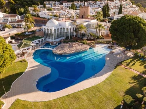 Vista aérea del lujoso apartamento Nerja Holiday Homes con piscina azul curva, edificio de cúpula blanca y vistas al Mediterráneo