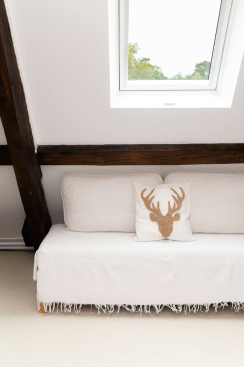 Cosy chambre aux Lodges de la Ferme de la Chaise avec canapé crème, coussin bois de cerf et vue sur les jardins par lucarne