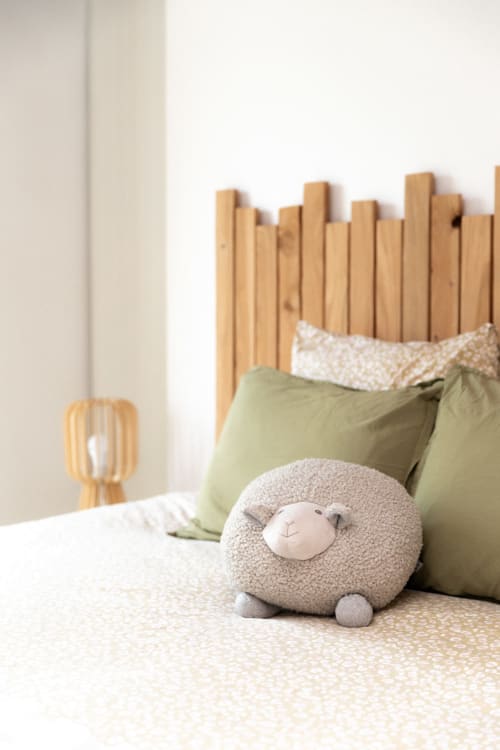 Lit douillet avec tête de lit en bois, oreillers verts et jouet mouton moelleux à la Ferme de la Chaise