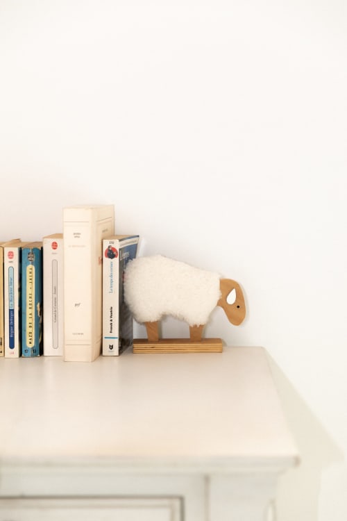 Figurine de mouton en bois à laine blanche posée près de livres sur une étagère à la Ferme de la Chaise