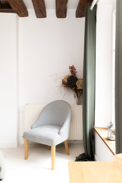 Chaise grise rembourrée avec pieds en bois dans la chambre Goupil aux Lodges de la Ferme de la Chaise