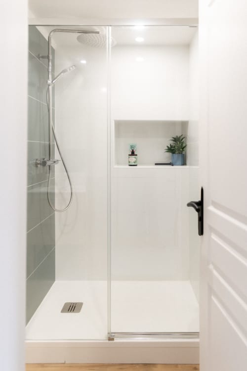 Salle de bain moderne avec douche à l'italienne, carrelage blanc, pommeau de douche cascade et niche intégrée avec plante aux Lodges de la Ferme de