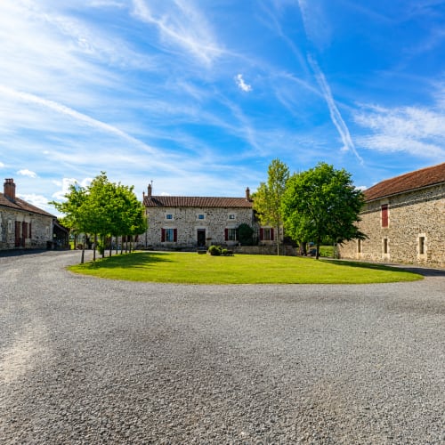 Cour en pierre du gîte Domaine de Beau Site à Peyrat-de-Bellac, avec pelouse verte et bâtisses rustiques