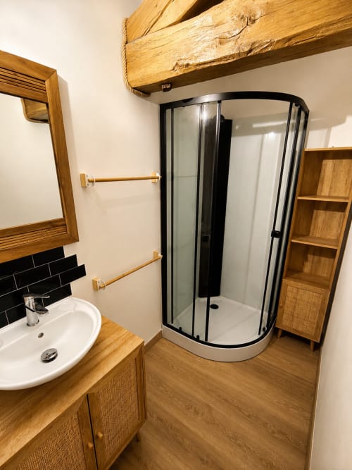 Modern bathroom in Le Grand Gîte cottage at Domaine de Beau Site, featuring wooden beams, curved shower enclosure, and vanity