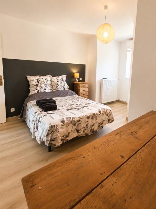 Spacious bedroom at Domaine de Beau Site cottage with black accent wall, patterned bedding, wooden furniture, and pendant