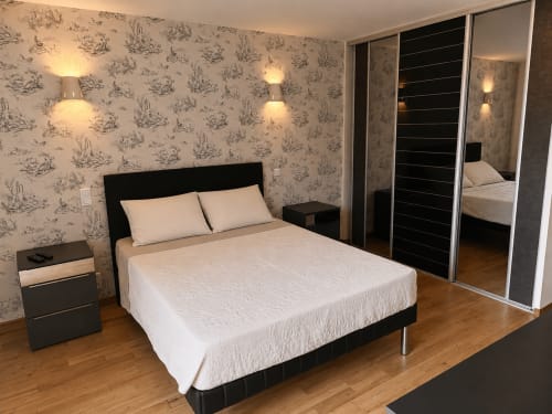 Modern bedroom at Domaine de Beau Site cottage with queen bed, black headboard, patterned wallpaper, and mirrored wardrobe