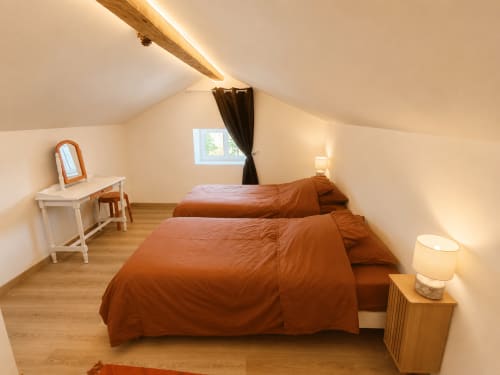 Attic bedroom at Domaine de Beau Site with two beds, wooden beams, and garden view window