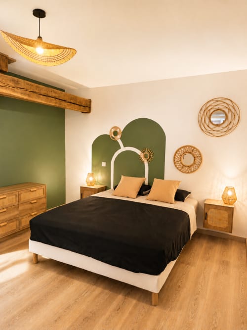 Modern cottage bedroom at Domaine de Beau Site with green accent wall, wooden furnishings, and woven decorative elements