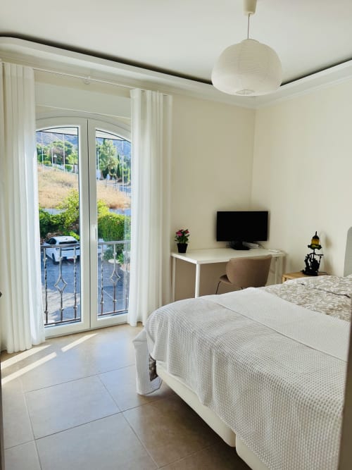 Dormitorio luminoso con cama blanca, escritorio con TV y puertas de cristal con vistas al mar en villa Nerja Holiday Homes