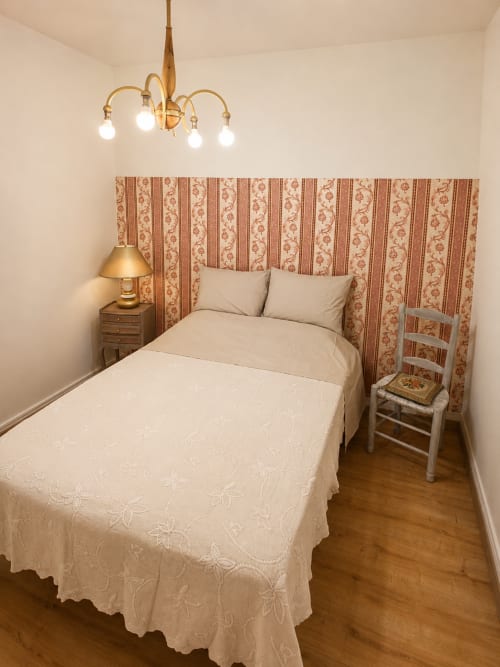 Cozy bedroom at Domaine de Beau Site cottage with cream bedding, patterned headboard, brass chandelier, and wooden floors.
