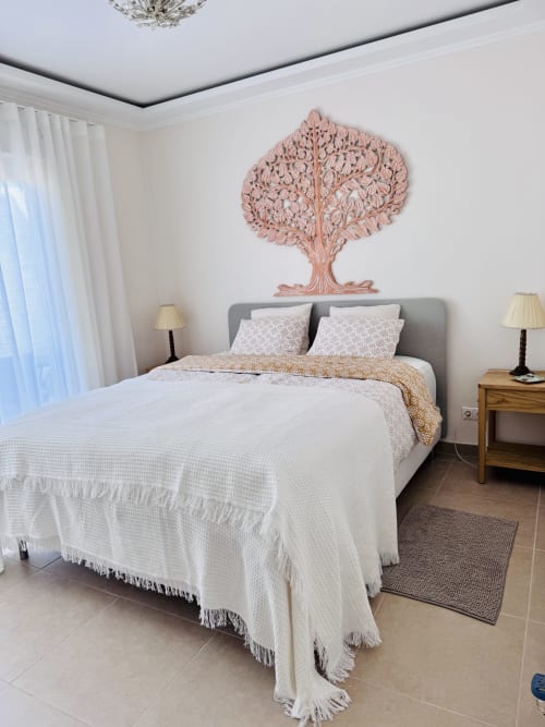 Dormitorio moderno en villa de Nerja con cama tapizada gris, arte mural de árbol rosa, ropa de cama blanca y mesitas de noche gemelas con lámparas