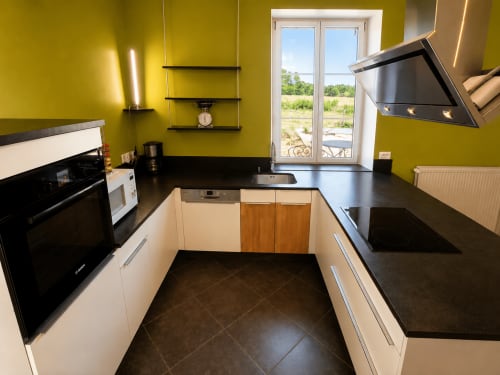 Modern kitchen in Le Grand Gîte cottage at Domaine de Beau Site with yellow walls, black countertops, and garden view windows