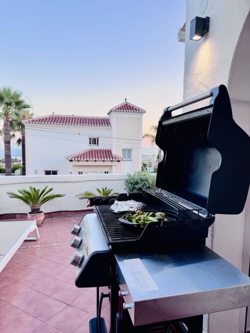 Parrilla de gas negra en terraza con vistas al mar de villa en Nerja, arquitectura mediterránea al fondo