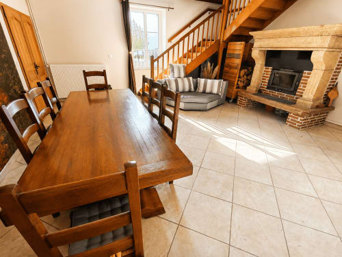 Open-plan living area at Le Grand Gîte cottage with wooden dining table, fireplace, and staircase