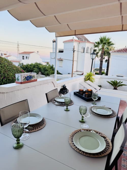 Elegante comedor en terraza de villa Nerja Holiday Homes con vistas al mar, platos blancos y copas verdes frente a la costa española