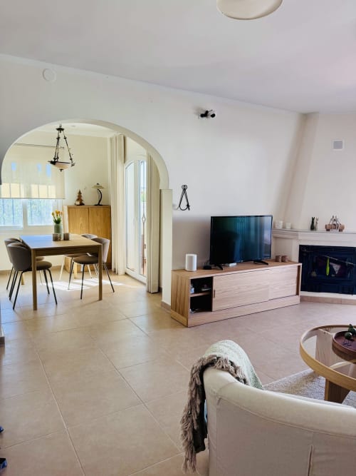 Sala de estar diáfana en villa de Nerja con TV, muebles de madera, mesa de comedor y vistas al mar a través de arco