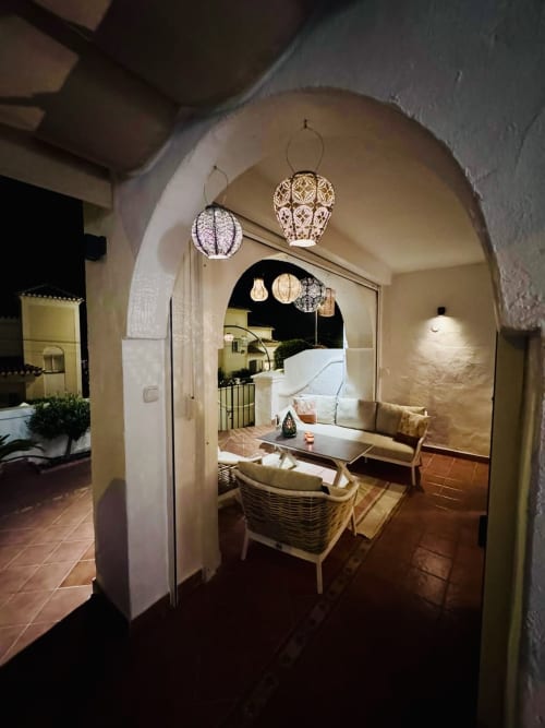 Elegante entrada con arco a villa en Nerja con lámparas colgantes decorativas, mobiliario de mimbre y vista de terraza nocturna