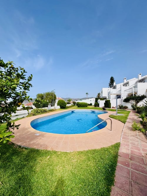 Piscina ovalada con agua azul rodeada de terraza de terracota y jardines cuidados en la villa Nerja Holiday Homes en España