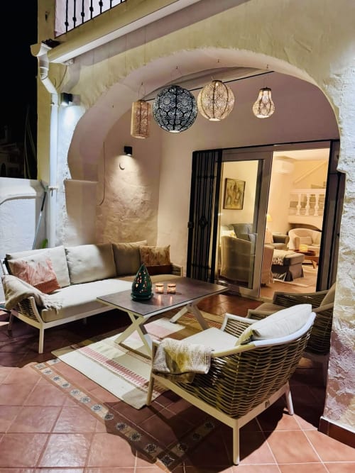 Elegante zona de descanso en terraza de villa nerjeña con techo de piedra abovedado, muebles de mimbre y linternas colgantes con vistas