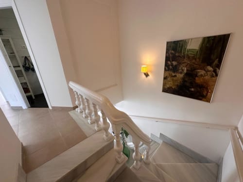 Escalera moderna con barandillas blancas en villa de Nerja, con obras de arte e iluminación ambiental en el pasillo